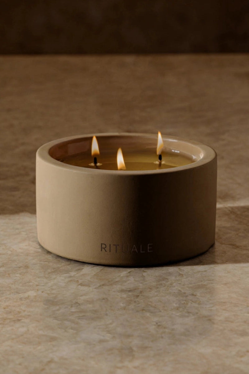Rituale three-wick concrete candle burning on marble surface with warm ambient background