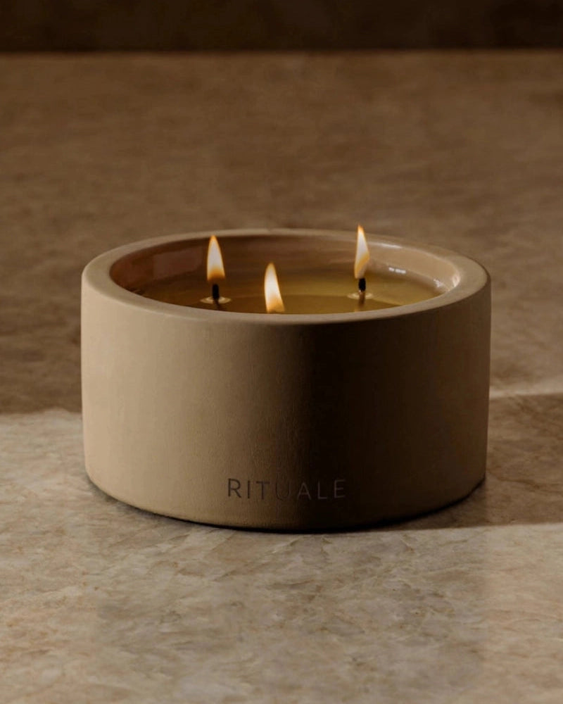 Rituale three-wick concrete candle burning on marble surface with warm ambient background