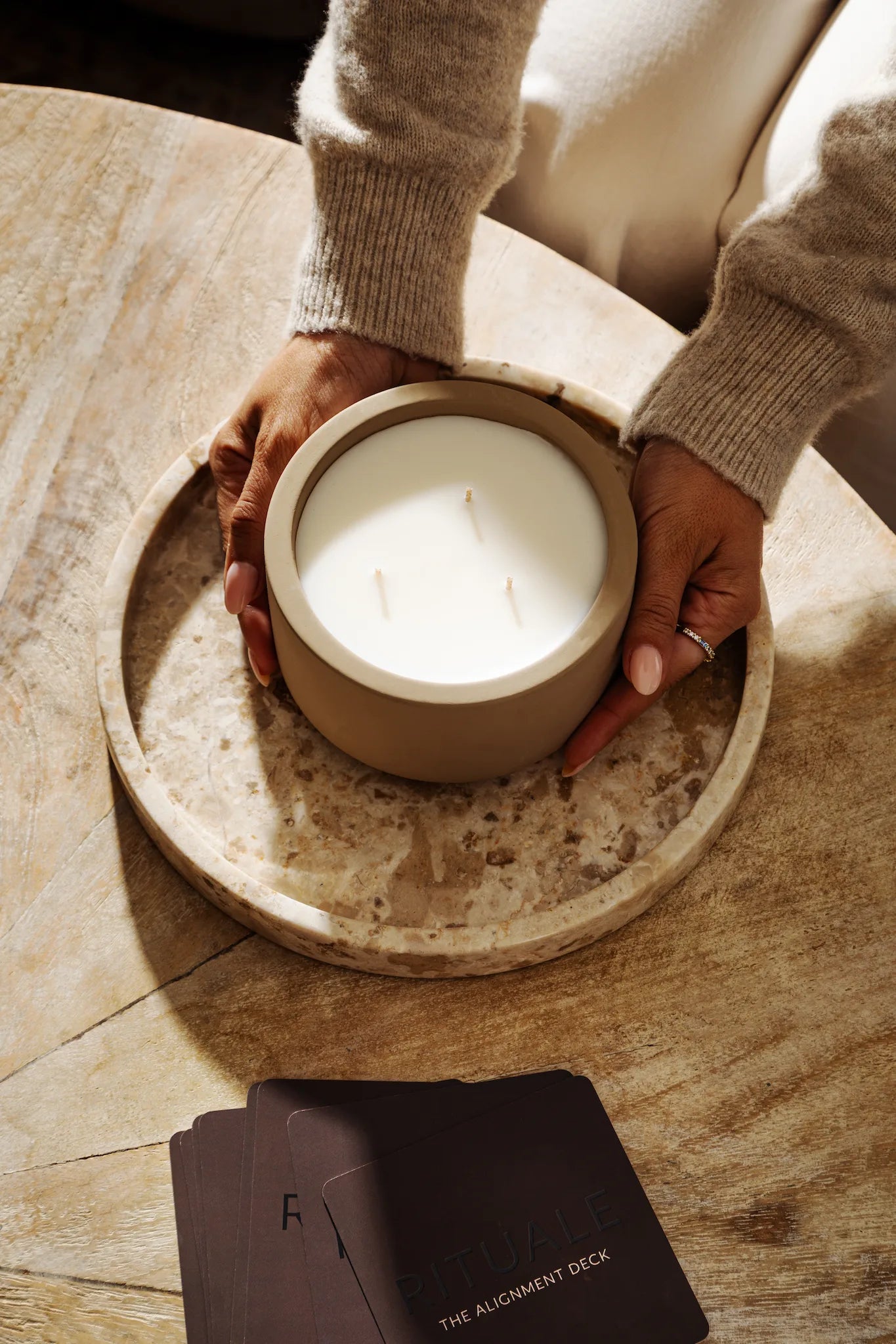 Hands cradling unlit Rituale concrete candle on marble tray atop wooden table