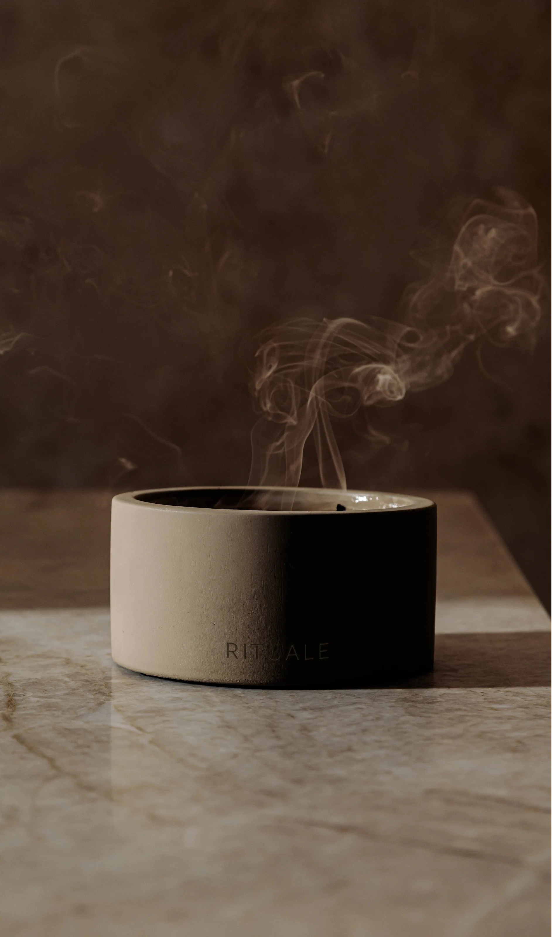 Rituale concrete candle freshly extinguished with smoke rising on marble surface
