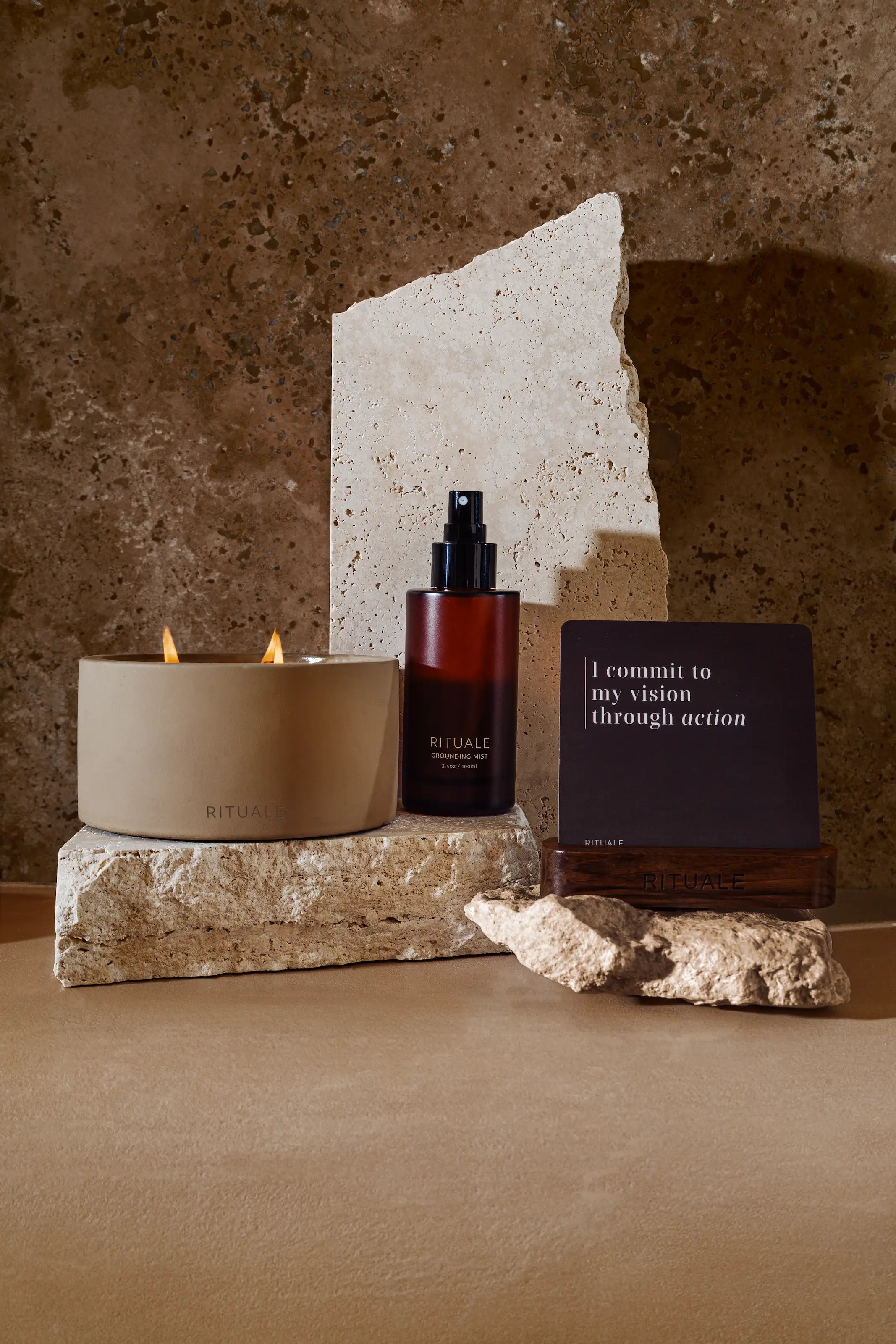 Rituale candle, grounding mist and alignment deck displayed on travertine stone against textured wall