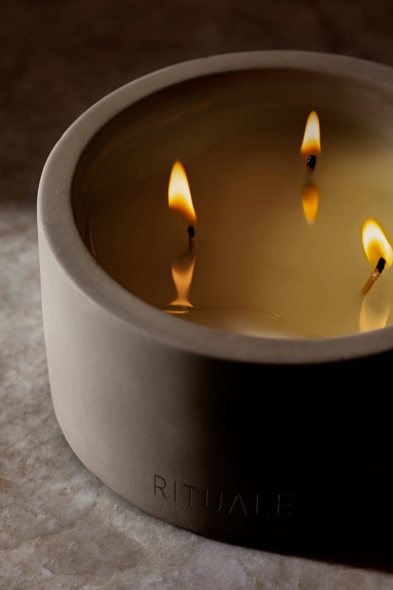Rituale three-wick concrete candle burning with three flames against marble background