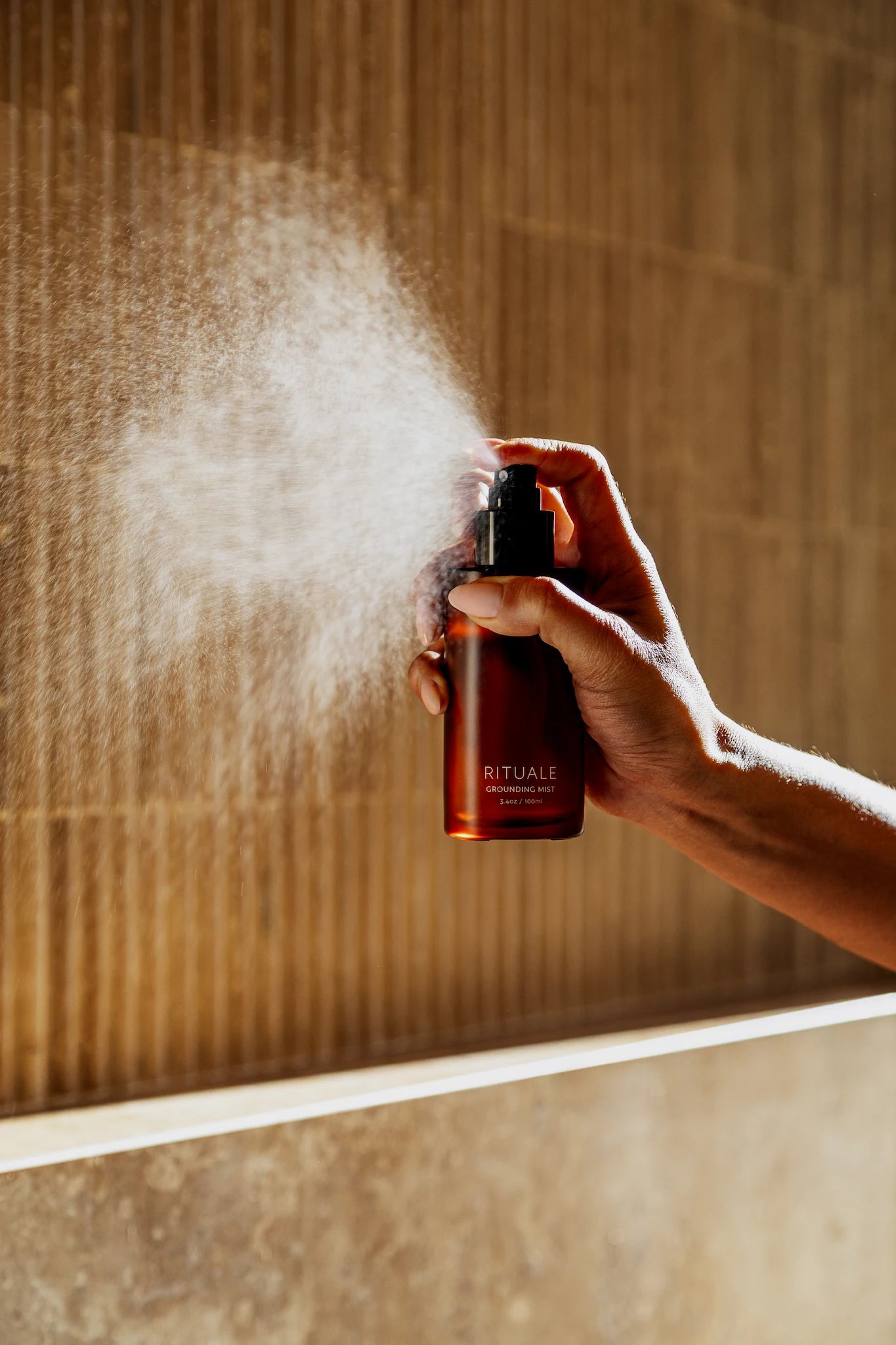 Hand spraying Rituale Grounding Mist against warm fluted tile wall