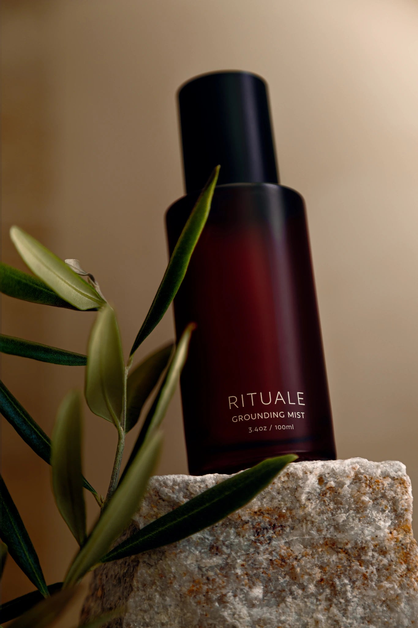 Rituale Grounding Mist bottle on stone surface with olive branch and soft neutral background