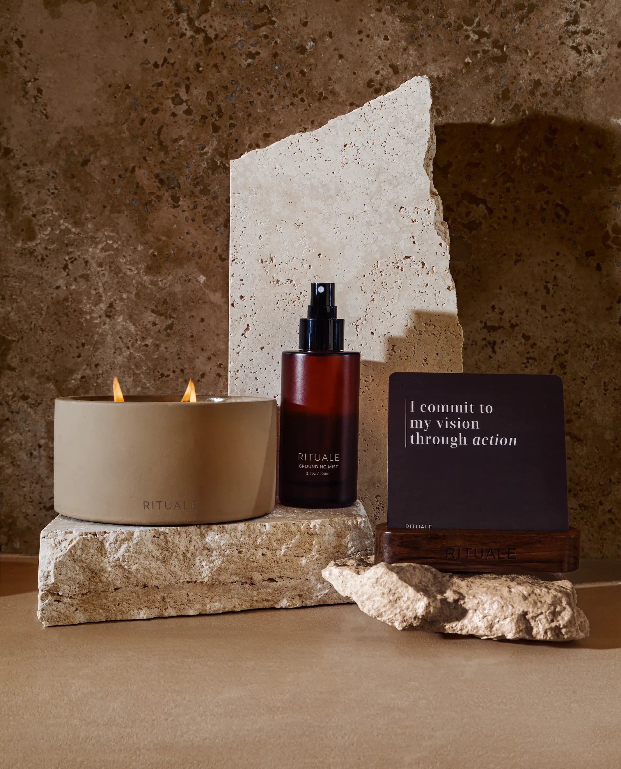 Rituale candle, grounding mist and alignment deck displayed on travertine stone against textured wall